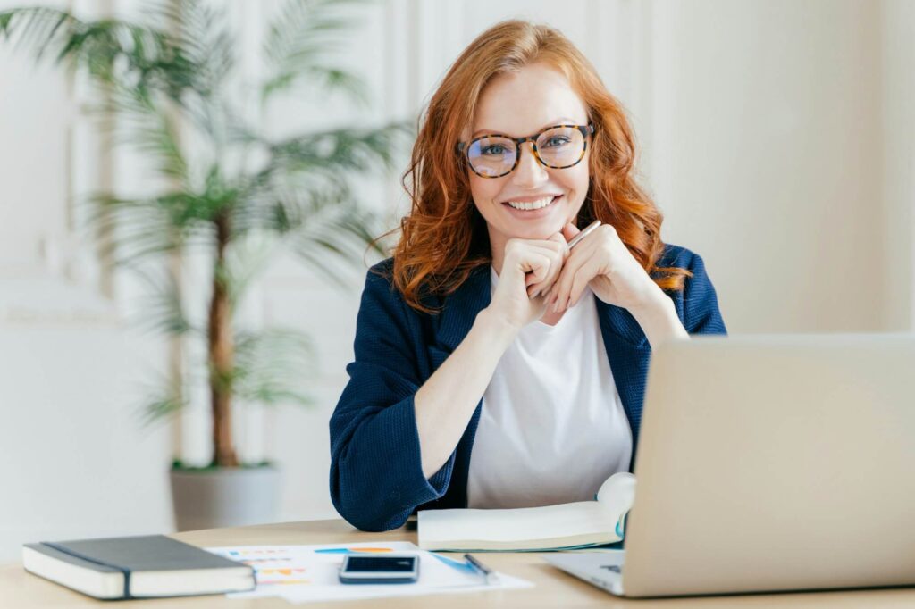 Home 1 pleased cheerful female economist develops financial startup project poses in office interior